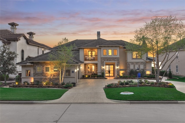 view of front of house with stucco siding, a balcony, stone siding, and a tiled roof