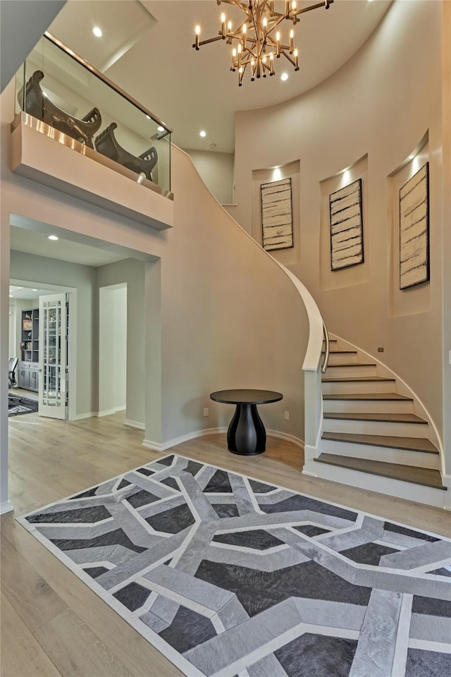 staircase featuring recessed lighting, a towering ceiling, wood finished floors, baseboards, and a chandelier