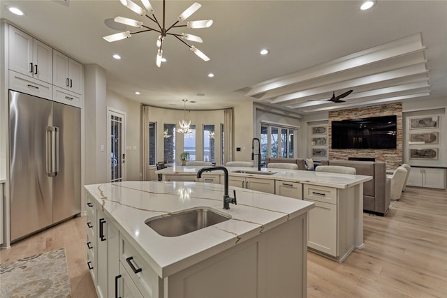 kitchen featuring high quality fridge, a sink, light wood-type flooring, recessed lighting, and an island with sink