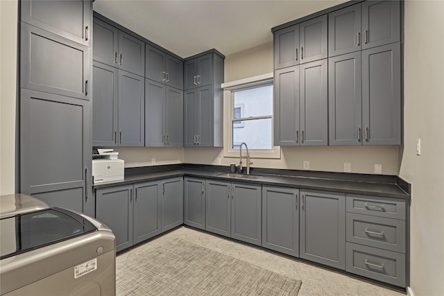 kitchen featuring a sink, dark countertops, stove, gray cabinets, and washer / dryer