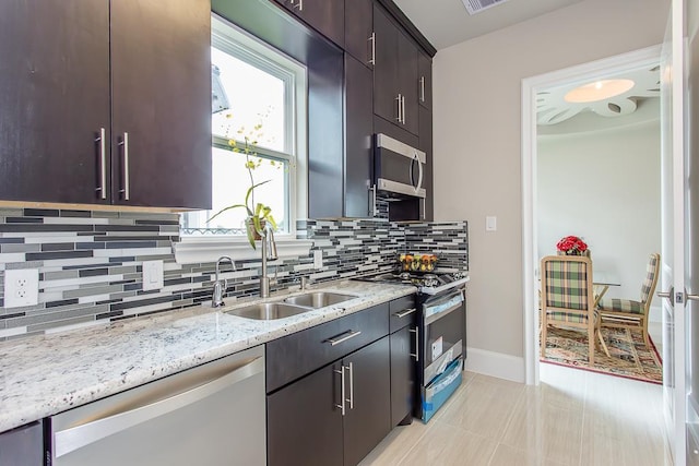 kitchen featuring light tile patterned floors, tasteful backsplash, a sink, appliances with stainless steel finishes, and light stone countertops