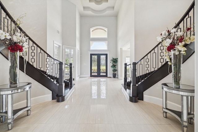 tiled entryway featuring baseboards, plenty of natural light, stairs, and a towering ceiling