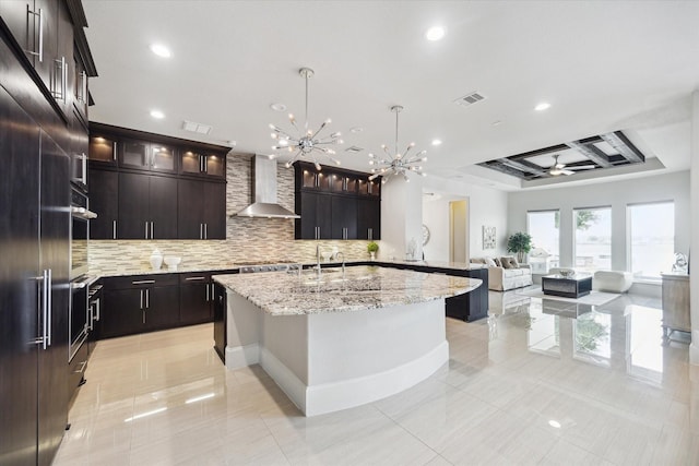 kitchen featuring recessed lighting, light tile patterned floors, backsplash, wall chimney range hood, and an island with sink