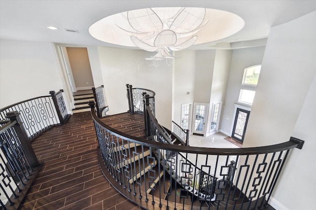 staircase featuring wood tiled floor, a high ceiling, visible vents, and baseboards