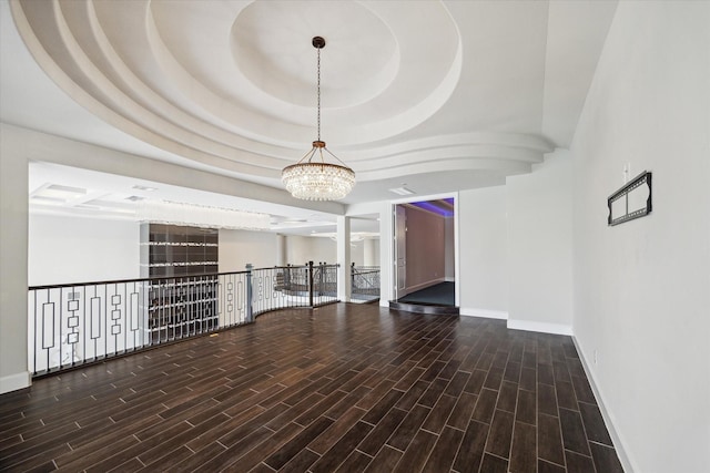 unfurnished room featuring a tray ceiling, an inviting chandelier, wood finished floors, and baseboards