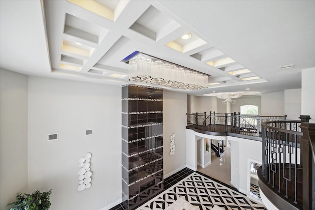 interior space featuring coffered ceiling, an upstairs landing, baseboards, visible vents, and beam ceiling