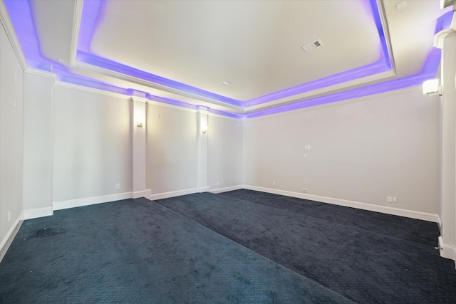 spare room with dark colored carpet, a raised ceiling, visible vents, and baseboards