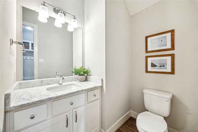 bathroom with vanity, toilet, vaulted ceiling, baseboards, and wood finished floors