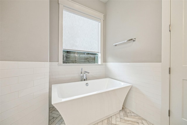 bathroom featuring tile walls, marble finish floor, wainscoting, and a soaking tub