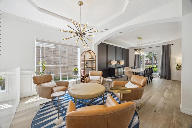interior space featuring an inviting chandelier, a raised ceiling, visible vents, arched walkways, and light wood-style flooring