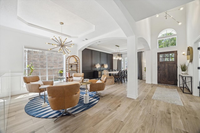 entryway with arched walkways, a tray ceiling, light wood-style flooring, and an inviting chandelier