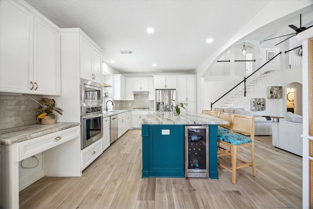 kitchen with a sink, beverage cooler, ceiling fan, arched walkways, and stainless steel appliances