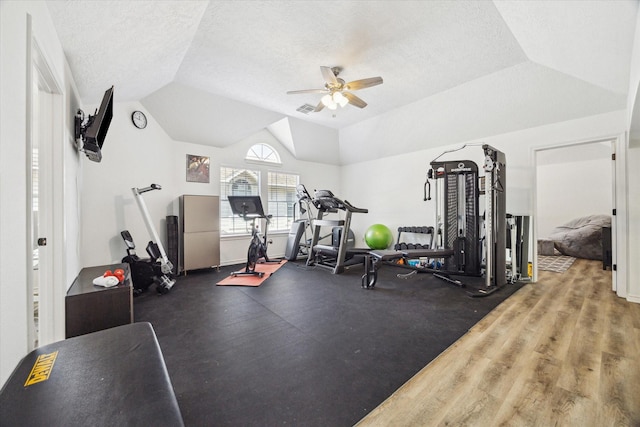 exercise area featuring vaulted ceiling, a ceiling fan, a textured ceiling, and visible vents
