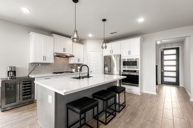 kitchen featuring a sink, appliances with stainless steel finishes, visible vents, under cabinet range hood, and wine cooler
