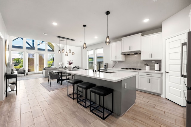 kitchen with stainless steel gas stovetop, under cabinet range hood, light countertops, a sink, and open floor plan