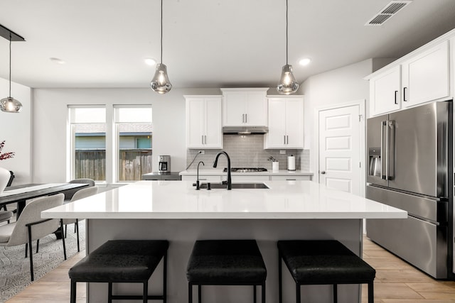 kitchen featuring high end fridge, a sink, a breakfast bar, backsplash, and under cabinet range hood