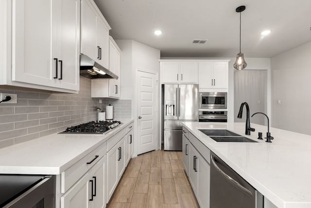 kitchen featuring a sink, light wood-style floors, stainless steel appliances, under cabinet range hood, and visible vents