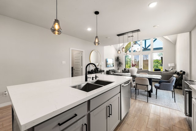 kitchen featuring light wood finished floors, a sink, open floor plan, dishwasher, and an island with sink