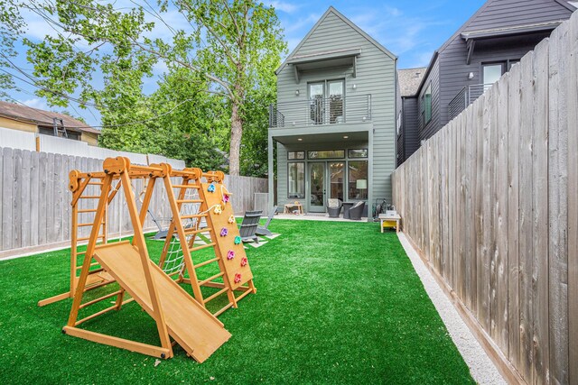 back of house featuring a fenced backyard, a playground, a balcony, a yard, and a patio