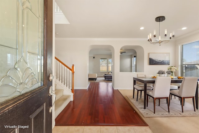 dining area with arched walkways, ornamental molding, a chandelier, stairs, and healthy amount of natural light