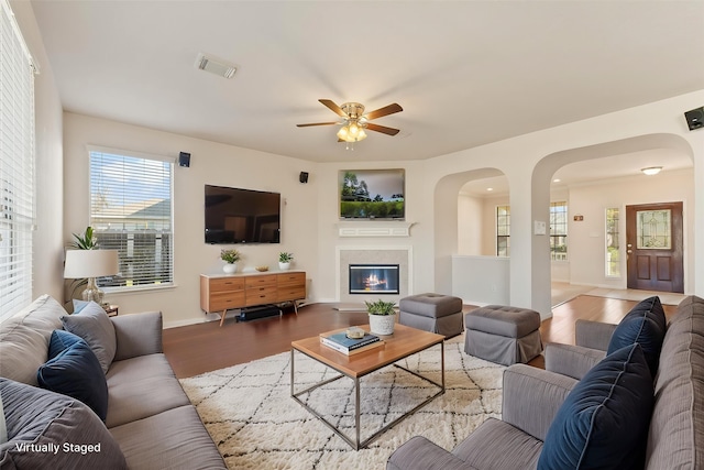 living area featuring wood finished floors, a ceiling fan, arched walkways, baseboards, and a glass covered fireplace