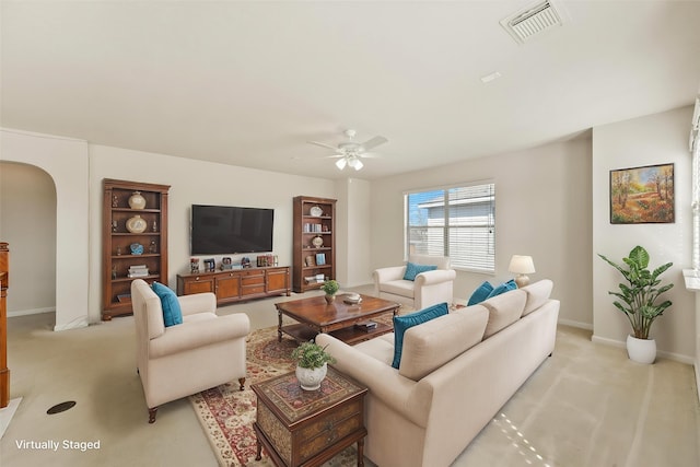 living area featuring arched walkways, light colored carpet, ceiling fan, and baseboards