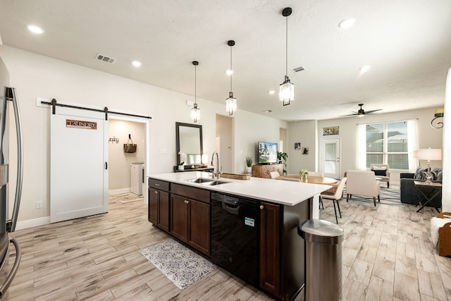 kitchen with a sink, a barn door, open floor plan, visible vents, and black dishwasher