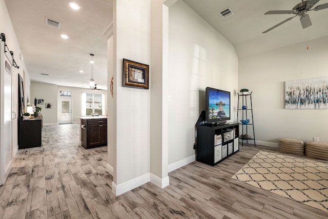 hall with baseboards, visible vents, light wood-style floors, and a barn door
