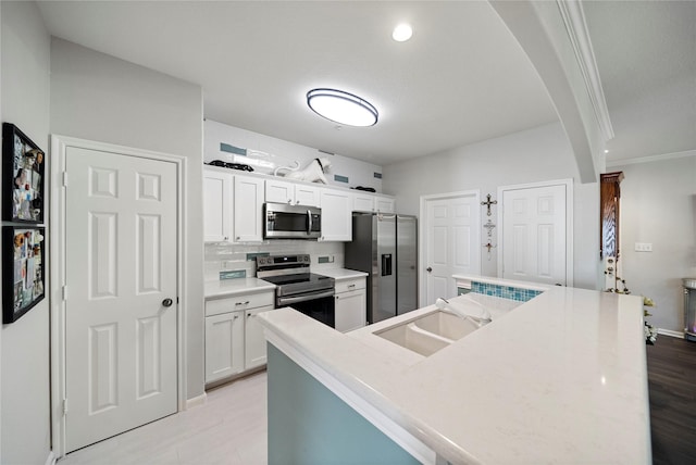 kitchen with white cabinets, stainless steel appliances, a sink, arched walkways, and decorative backsplash