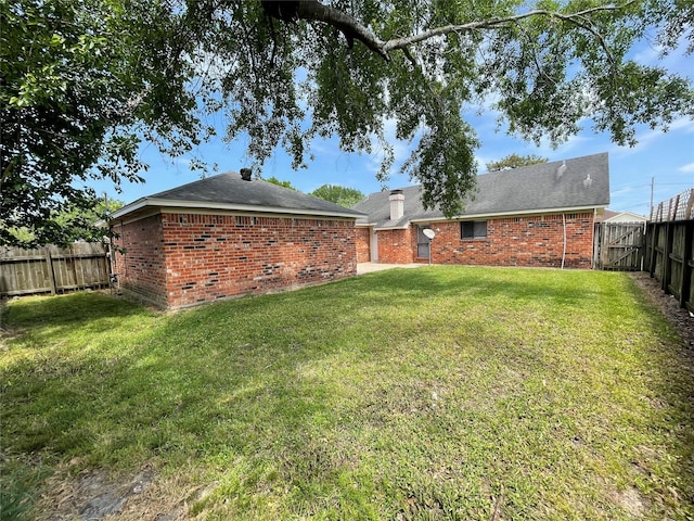 back of property with brick siding, a yard, a chimney, and a fenced backyard
