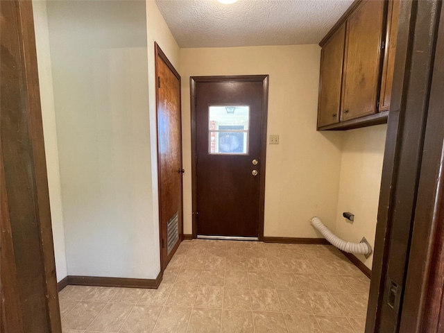 clothes washing area featuring cabinet space, a textured ceiling, baseboards, and light tile patterned flooring