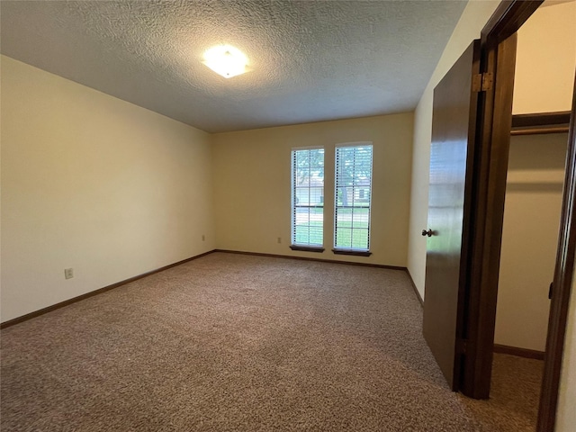 empty room with light colored carpet, baseboards, and a textured ceiling
