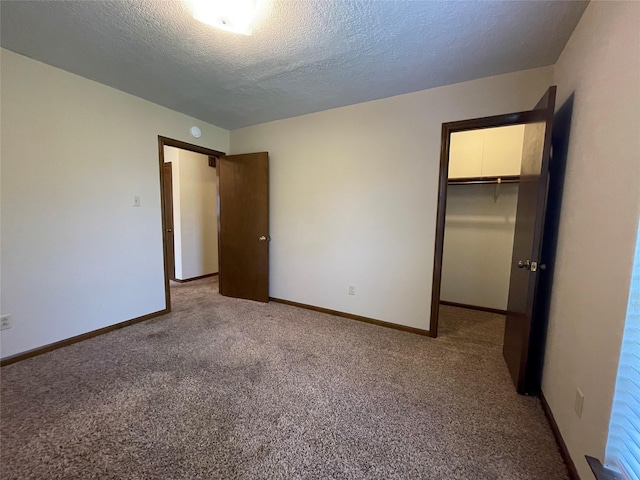 unfurnished bedroom featuring a textured ceiling, a closet, a spacious closet, baseboards, and carpet flooring