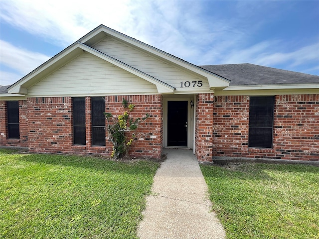 single story home with brick siding, a shingled roof, and a front yard