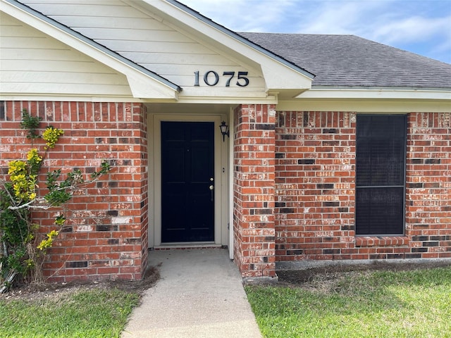 property entrance featuring brick siding and a shingled roof