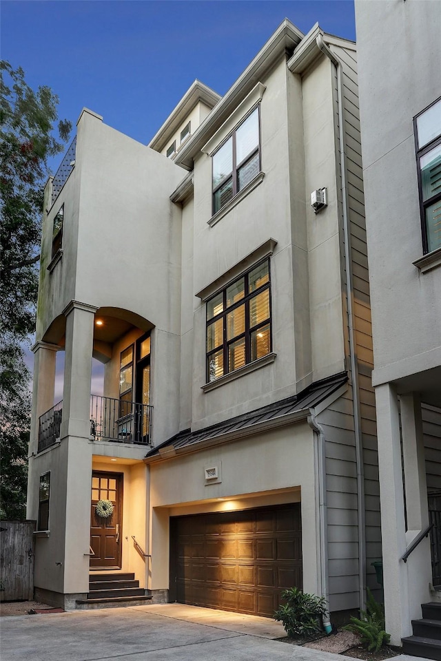 view of front of property with an attached garage, a balcony, stucco siding, metal roof, and a standing seam roof