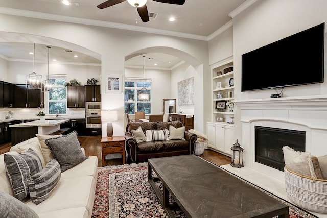 living area with ceiling fan with notable chandelier, dark wood-type flooring, visible vents, crown molding, and arched walkways