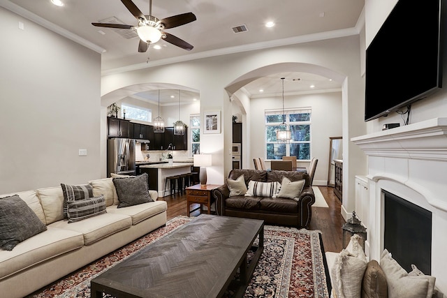 living area with ceiling fan with notable chandelier, dark wood-type flooring, visible vents, and arched walkways