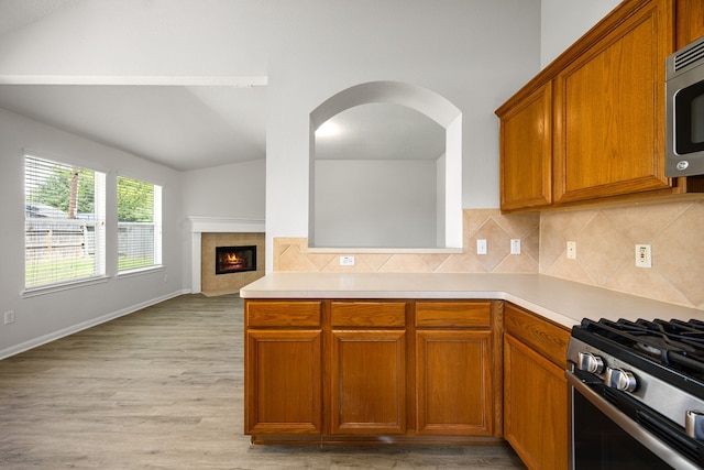 6723 Cypress Glades Dr, Katy, TX 77449 - kitchen featuring brown cabinets, lofted ceiling, stainless steel appliances, light countertops, and a tiled fireplace