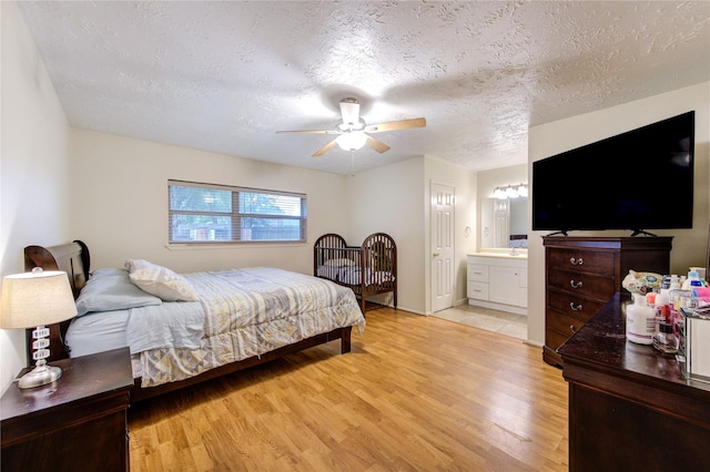 bedroom featuring a ceiling fan, a textured ceiling, ensuite bathroom, and light wood-style flooring
