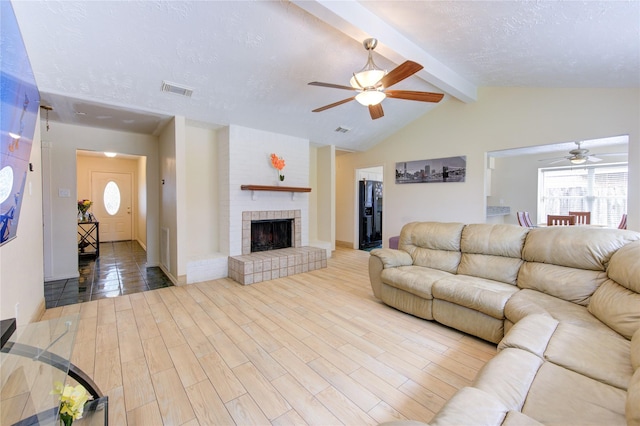 living area with vaulted ceiling with beams, visible vents, a fireplace, and ceiling fan