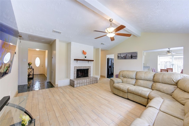 living area with ceiling fan, lofted ceiling with beams, a textured ceiling, and visible vents