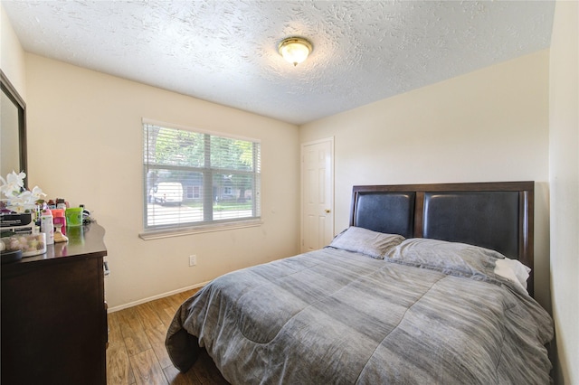 bedroom with baseboards, wood finished floors, and a textured ceiling