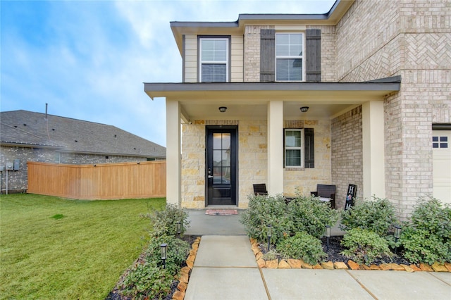 doorway to property featuring a lawn, fence, and a porch