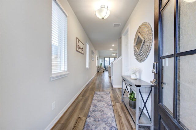 hallway with baseboards, wood finished floors, and visible vents