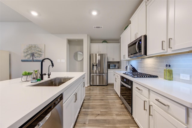 kitchen featuring white cabinets, stainless steel appliances, light wood-style flooring, a sink, and light countertops
