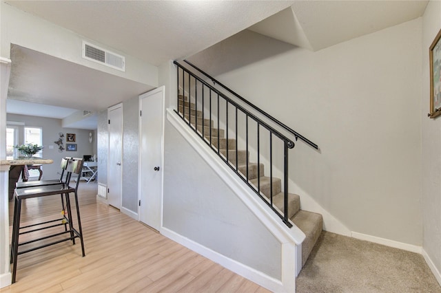 staircase featuring wood finished floors, visible vents, and baseboards