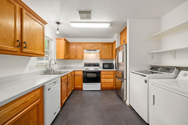 kitchen featuring visible vents, white appliances, under cabinet range hood, washing machine and clothes dryer, and a sink