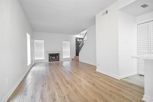 unfurnished living room with light wood-type flooring, baseboards, visible vents, a premium fireplace, and stairway