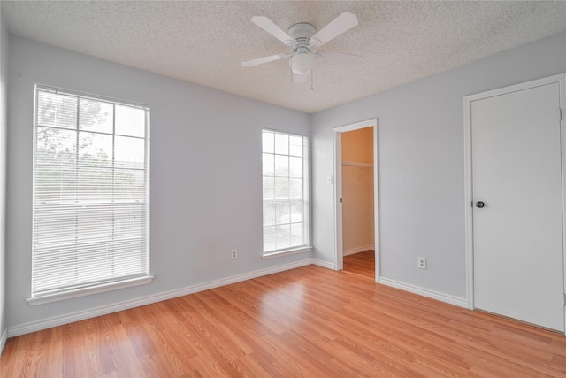 empty room with a ceiling fan, baseboards, a textured ceiling, and light wood-style floors